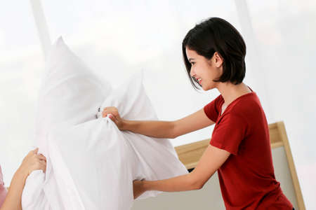 Happy young couple friend beautiful asia women having a pillow fight in their bedroom.の写真素材