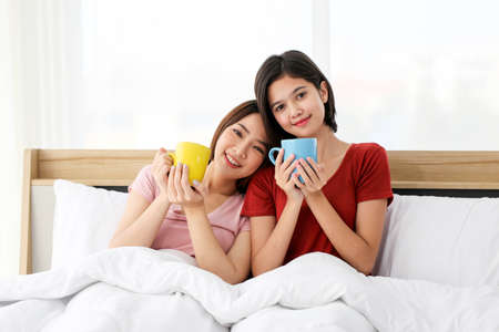 Happy Couple  asia woman enjoy together with drink morning coffee, fresh tea or hot milk in cup on the bed in morning.の写真素材