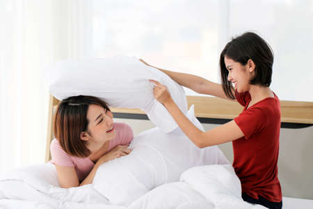 Happy young couple friend beautiful asia women having a pillow fight in their bedroom.の写真素材