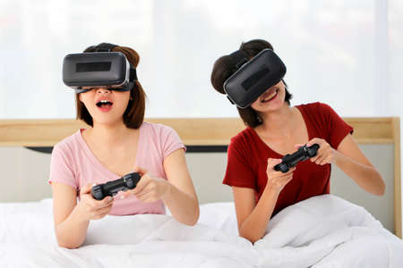 Happy young couple friend beautiful asia women playing video games virtual reality glasses on the bed in a bedroom,Gaming conceptの写真素材