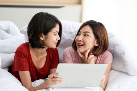 Happy Couple  asia woman wear headphones and enjoy musics playing mobile phone and tablet in bedroom.の写真素材