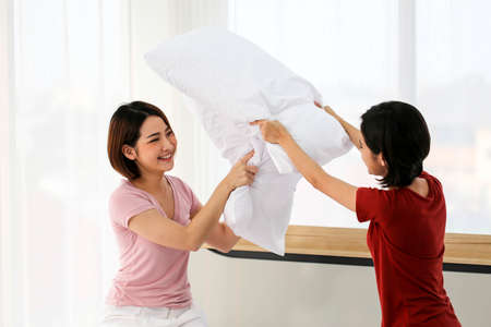 Happy young couple friend beautiful asia women having a pillow fight in their bedroom.の写真素材