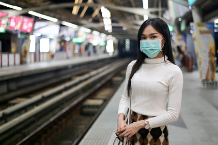 Beautiful asia woman looking at watch standing in lines waiting sky train on platform at night.の写真素材