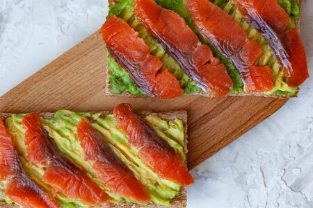 Two sandwiches with red fish and avocado on wooden cutting boardの写真素材