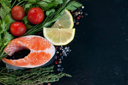 a fresh salmon steak with greenery, lemon and cherry tomatoes on the black boardの写真素材