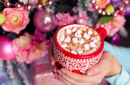a cup of aromatic cocoa with marshmellow in the hands just before christmas eve