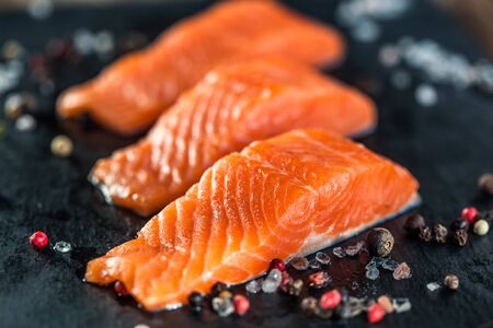 Three salmon steakes with pepper and salt grains on the black boardの写真素材