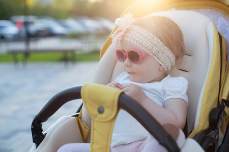 Baby girl seating in stroller, wearing sunglasses and floral headband
