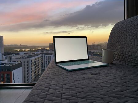 Opened laptop on grey sofa with panoramic view of night city from the windowの写真素材