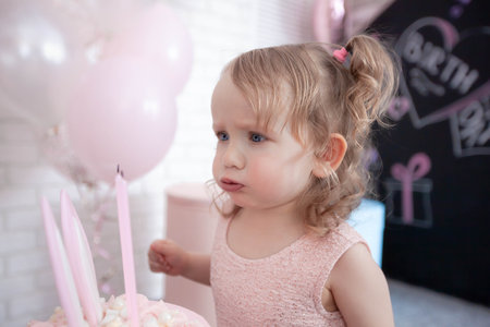 little girl blowing out burning candles on her birthday cakeの写真素材