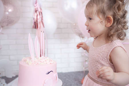 little girl blowing out burning candles on her birthday cakeの写真素材