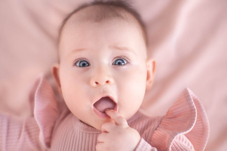 Portrait of a blue-eyed 6 months baby girl with finger in mouthの写真素材
