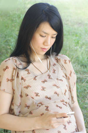 Pregnant Asian woman listening the music with earbuds
