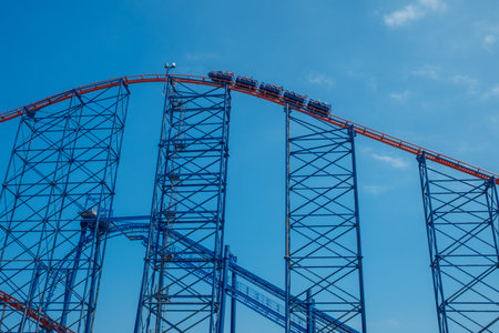 A towering blue roller coaster against a clear sky, capturing the excitement and engineering marvel of amusement parks. Perfect for themes of leisure, adventure, and family fun.の写真素材
