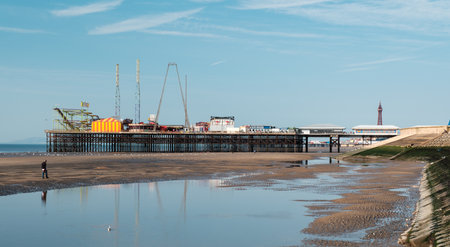 Serene beachscape with a vibrant pier and reflective wet sand under a clear blue sky.