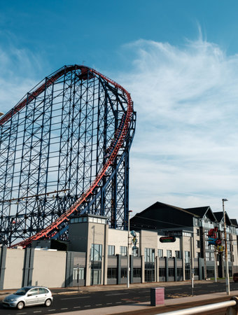 A towering roller coaster looms over urban architecture under a clear blue sky.
