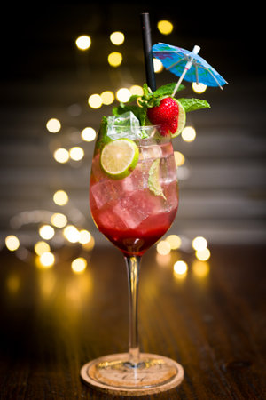 Strawberry soda with mint leaves filling, with slices of lime and small umbrella decoration, on blurred lights backgroundの写真素材