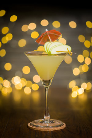 Apple martini in glass with slices of apple and small umbrella decoration, on blurred lights backgroundの写真素材