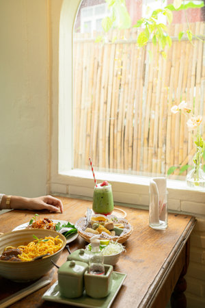 Various food on wooden table beside window with matcha drinksの写真素材