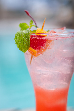 Close up of Singapore sling cocktails in glass garnished with slice of lemon, sprig of mint and cocktail cherry. The glass sits on a wooden trayの写真素材