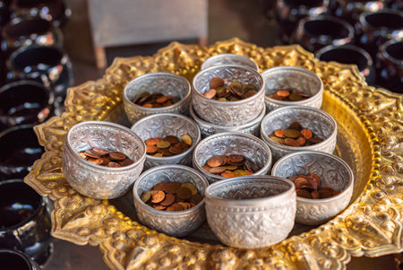 Close-up small silver bowls filled coins on golden tray in thai templeの写真素材