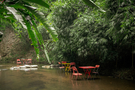 Serene outdoor scene featuring several small tables and chairs set up in shallow waterの写真素材