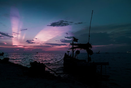 Silhouetted fishing boat near the shoreline in tranquil scene at dusk by the waterの写真素材