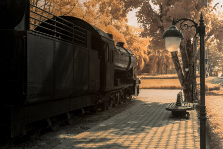 Infrered photography, a vintage steam locomotive parked beside a path. The train is largely black, with details suggesting an older styleの写真素材