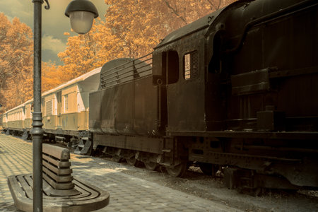 Infrered photography, a vintage steam locomotive parked beside a path. The train is largely black, with details suggesting an older styleの写真素材