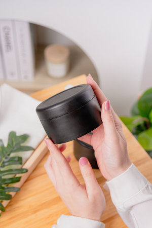 A person's hands holding a black cylindrical container with a light-colored wooden table in backgroundの写真素材