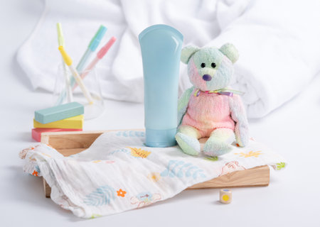 A light blue tube of lotion placed on a wooden tray with a soft, light-colored setting with various child-related itemsの写真素材
