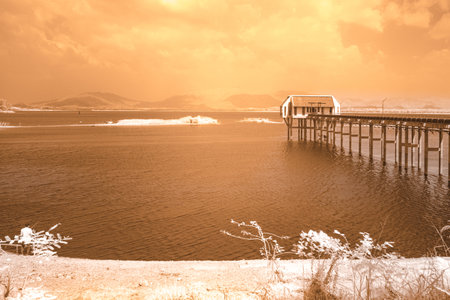 An infrared style, a body of water with a wooden pier and a structure at the endの写真素材