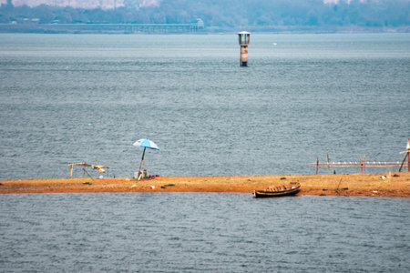 An infrared style, a tranquil water scene. In the foreground, there is a small sandy area surrounded by water. An umbrella sits on this sandy patch next to a small boatの写真素材