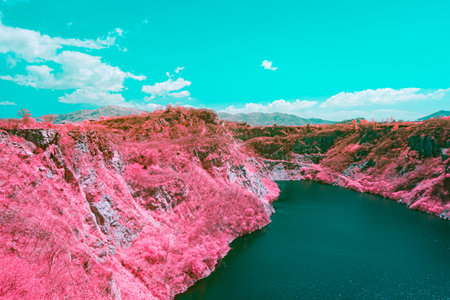 Infrared photography, a vast landscape featuring pink steep, rocky cliffs surrounding a greenish-blue body of water of quarryの写真素材