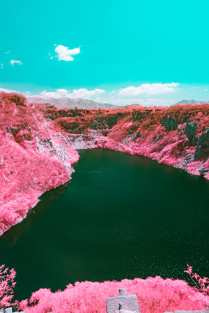 Infrared photography, a vast landscape featuring pink steep, rocky cliffs surrounding a greenish-blue body of water of quarryの写真素材