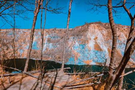 Infrared photography, a rocky landscape with steep walls surrounding a body of water and some bare trees in the foregroundの写真素材