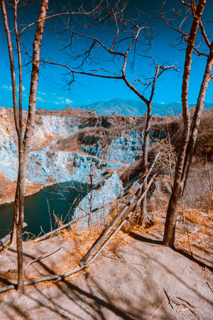 Infrared photography, a rocky landscape with steep walls surrounding a body of water and some bare trees in the foregroundの写真素材