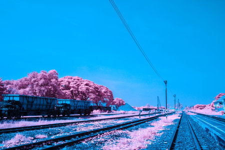 Infrared photography, a set of railroad tracks stretch out into the distance and a vibrant blue sky,...