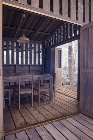 The interior of a simple wooden structure. Inside, there are several wooden chairs arranged around a tableの写真素材