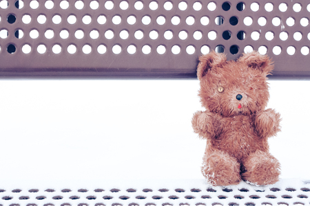 Worn out old teddy bear sitting on a bench in the snow.の写真素材
