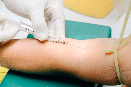 Doctor or nurse hands in medical blue gloves using needle syringe drawing blood sample from patient arm in hospital. Scientist get blood draw for hemoculture testing as specimen in research laboratoryの写真素材