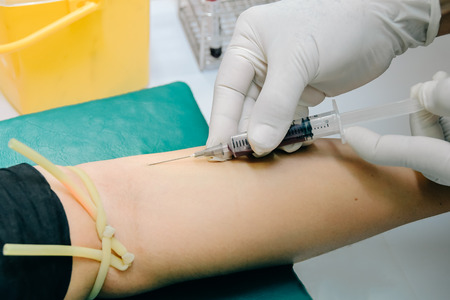 Doctor or nurse hands in medical blue gloves using needle syringe drawing blood sample from patient arm in hospital. Scientist get blood draw for hemoculture testing as specimen in research laboratoryの写真素材