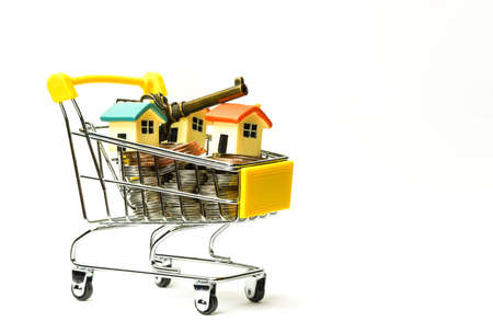 Tiny house with key on coins in a shopping cart. Isolated on white background. concept ideas. copy space, sale and purchase of real estateの写真素材