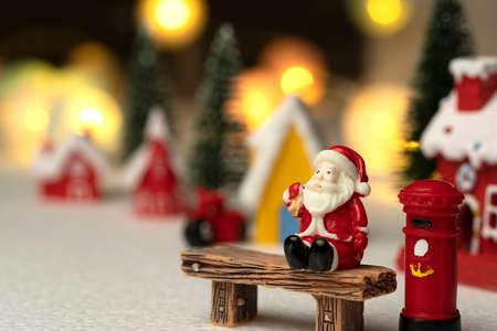 Santa Claus sits back and relax in front of mailbox with red and yellow hut with snow on the roof.の写真素材