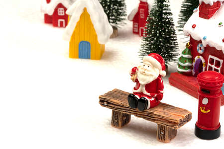 Santa Claus sits back and relax in front of mailbox with red and yellow hut with snow on the roof.の写真素材