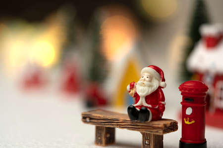 Santa Claus sits back and relax in front of mailbox with red and yellow hut with snow on the roof.の写真素材