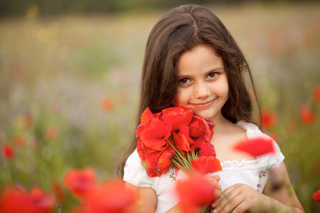A cute little girl in the field of poppies holding a bunch of flowersの写真素材