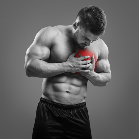 Muscular shirtless man with chest pain over gray background. Concept with highlighted glowing red spot.の写真素材