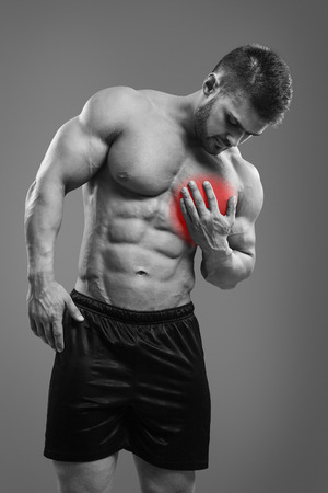 Muscular shirtless man with chest pain over gray background. Concept with highlighted glowing red spot.の写真素材