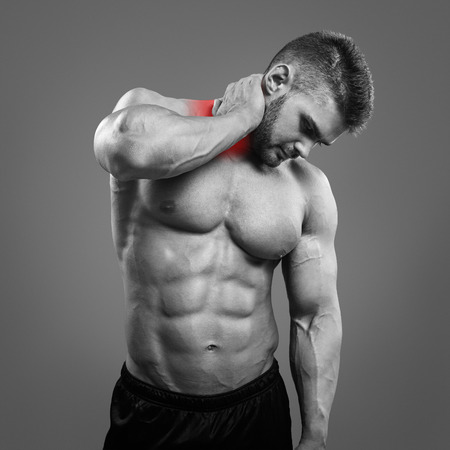 Muscular man suffering from neck pain. Front view over gray backgroundの写真素材